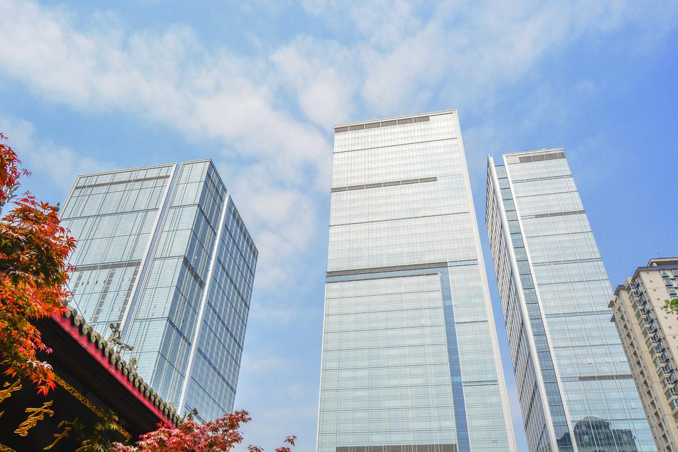 Shiny buildings near the beautiful and colorful temples corner with trees, under the blue sky with clouds