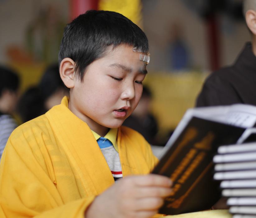 young buddhist monk with book on blurred background