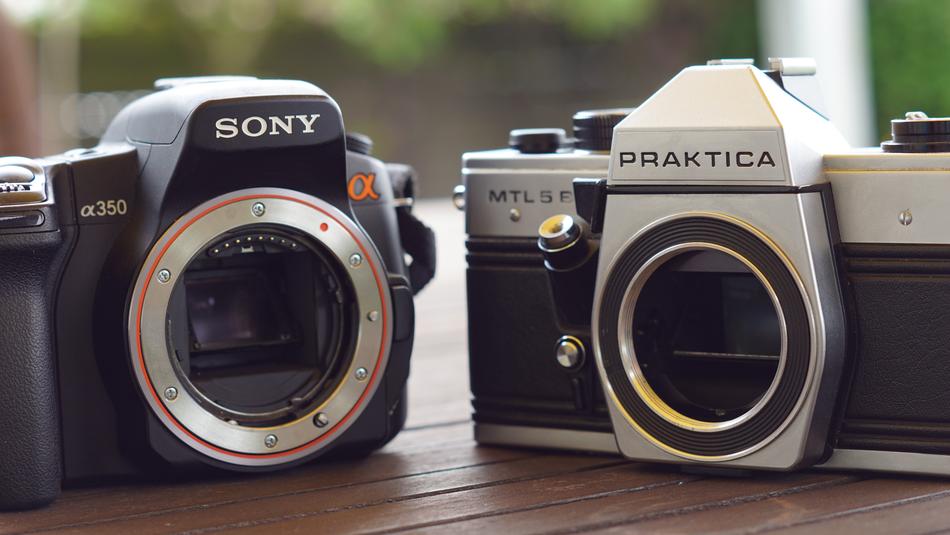 Old 'Sony' and 'Praktica' cameras on the wooden table, at blurred background