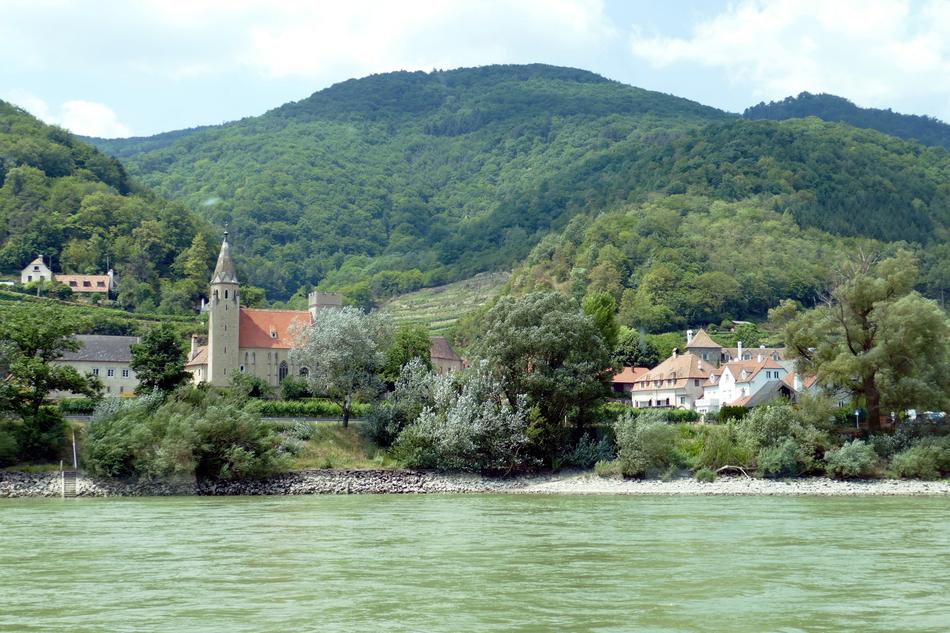 Beautiful and colorful church on the shore of the river, on the green mountains in Wachau in Austria
