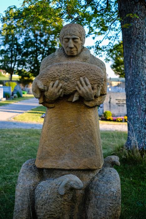 Beautiful sculpture of the man, among the colorful plants in the park