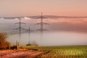 panoramic photo of agricultural field and high-voltage towers in morning fog