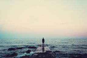Person, standing on the beautiful pier, among the water with waves, at colorful, gradient sunrise in the sky