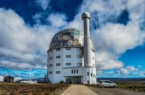 White observatory with shiny dome among the cars and colorful fields at blue sky with white clouds