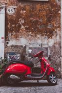 Beautiful, shiny, red Vespa motor scooter, near the sign, near the wall