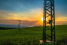 electric poles stand on a green background against the background of a bright sunset