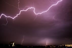 Beautiful, purple lightning, above the city with colorful lights, at night