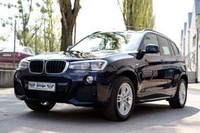 Beautiful, shiny black Bmw x3 car on the road, among the plants and buildings