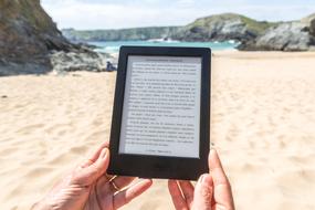 Reading, e-book in female hands at beach