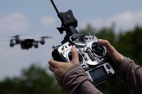 Person, controlling the flying drone, near the green trees