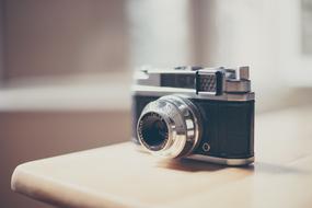 Close-up of the beautiful, shiny black and metallic, retro camera on the wooden table, in light