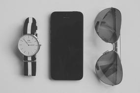 black and white photo of a watch, smartphone and sunglasses