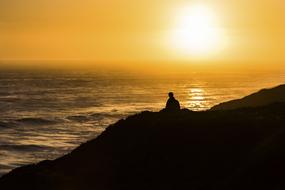 silhouette of a man on a hill by the sea during sunset