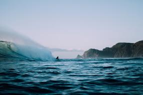 Beautiful landscape with the person, surfing on the turquoise and blue water, near the mountains