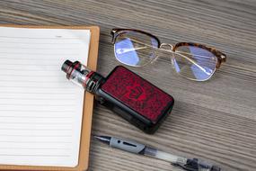 electronic cigarette, glasses, pen and open notebook