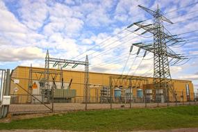 Switching station and high voltage line, near the green grass, under the blue sky, with white clouds