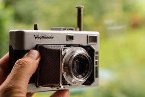 Grey and black, retro camera in the hand, in light, at blurred background with the colorful plants