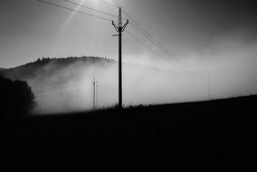 Black and white photo of the beautiful landscape with power lines in fog