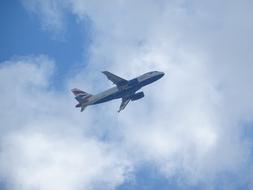 Flying aircraft of the British Airways, in the beautiful blue sky with white clouds