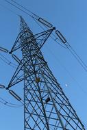 Low angle shot of an electricity tower with cables, at blue sky on background