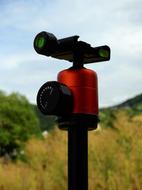 Red, black and green tripod for camera, among the beautiful, yellow and green fields on landscape
