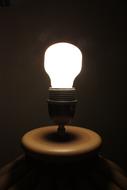 Close-up of the glowing light bulb, on the stand, among the darkness