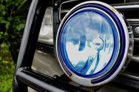 Close-up of the shiny, blue car headlight, near the colorful plants