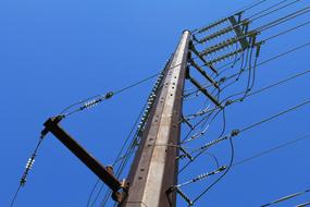 Low angle shot of the electrical poles, with the wires, under the blue sky