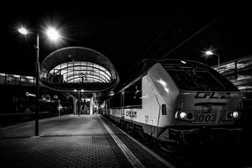 Black and white photo of the train, on the railway, on the railway station with lights