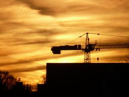 Silhouettes of the crane, building and trees, at beautiful, orange, yellow and golden sunset, with the clouds