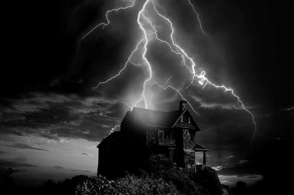 Black and white photo of the house, on the hill, under the cloudy sky with the flash in storm