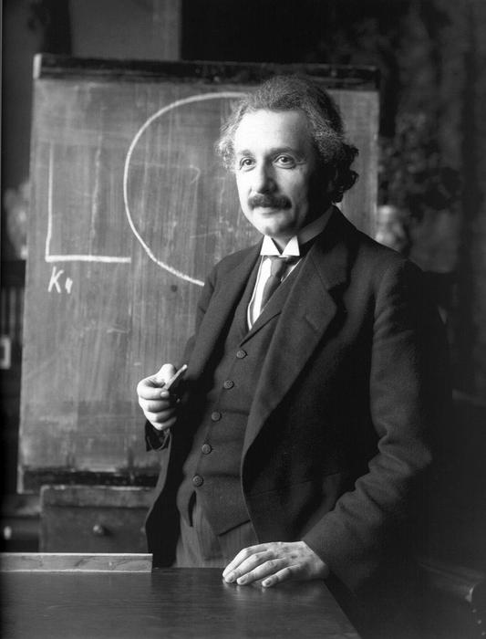 Black and white photo of Albert Einstein, near the blackboard, in the classroom