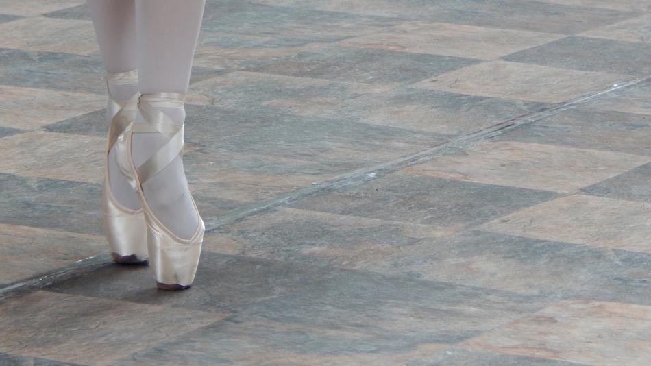 Beautiful, white feet of the ballerina, on the colorful pavement