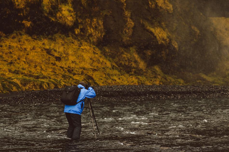 Person in blue jacket and with black backpack, near the beautiful river, among the colorful hills