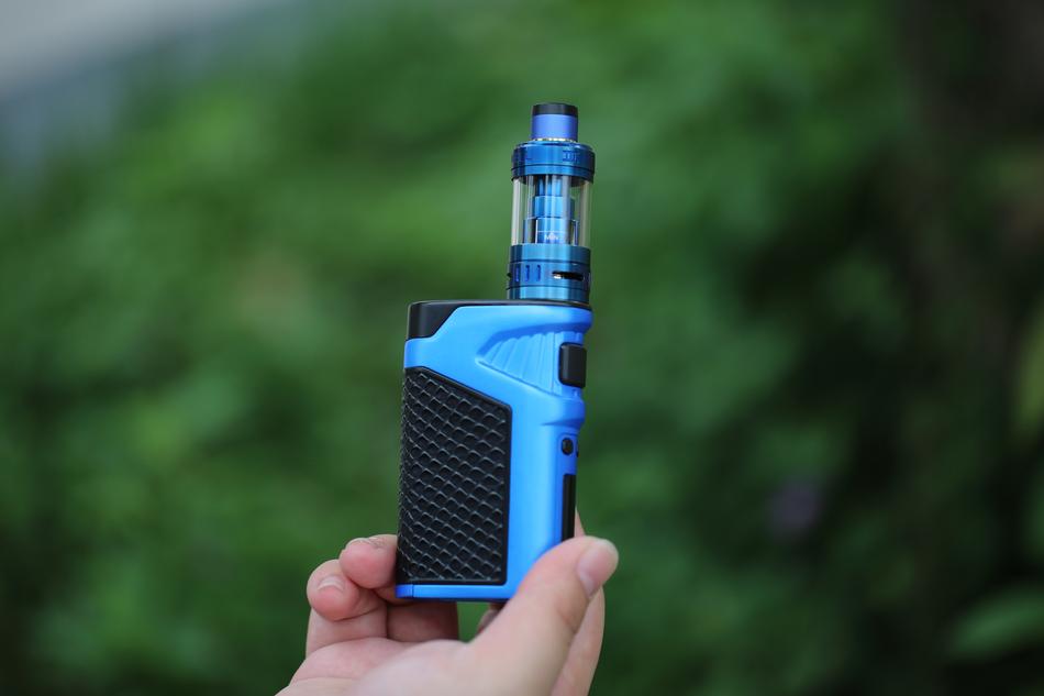 Blue and black 'Uwell' electronic cigarette in the hand, at blurred background with green plants