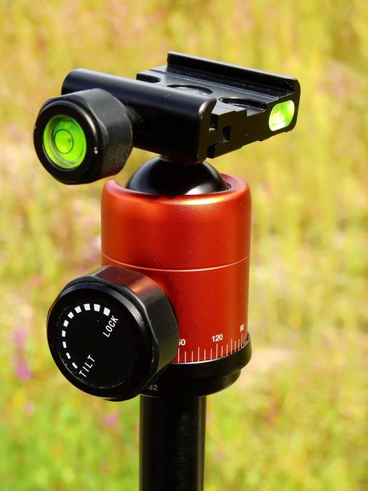 Close-up of the black camera on the black and red tripod, at background with colorful grass