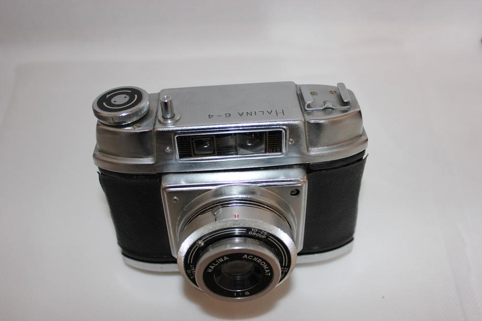 Top view of the shiny, metal and black 'Halina 6-4' camera, with the shadow, on the white surface