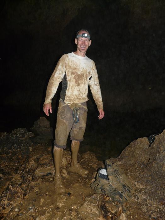 Smiling caver with lantern, in the dirty clothing, among the rocks