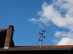 Close-up of the power lines on the roof of the house, at blue sky with white clouds on background