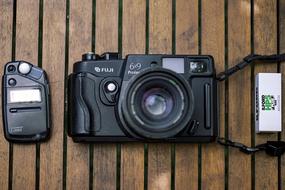 Close-up of the shiny, vintage, black camera, with the other devices, on the wooden surface