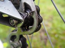 Close-up of the shiny, metal bike chain, at blurred background with the colorful grass