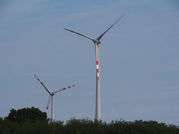 two gray wind turbines over green bushes