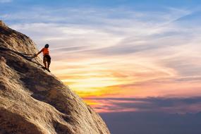 Climber on the mountain on colorful sky background with the clouds
