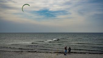 People, doing kite surfing on the beautiful beach of Baltic Sea, under the blue sky with clouds