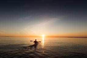 man with Paddle in Kayak on sea at sunset