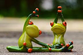 Cute, green and yellow frog figures with orange eyes and fingers, doing yoga