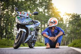 asian man in helmet sits on road beside of motorcycle