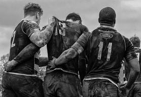 Black and white photo with the back view of the rugby players, in dirt