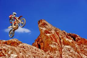 Rider in the helmet, jumping on the motorcycle, on the beautiful rocks, at blue sky with white clouds, on the motocross competition