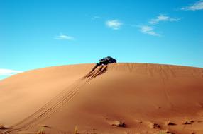 Rally car on the beautiful sand hill in the desert in Morocco, Africa, under the blue sky, with white clouds